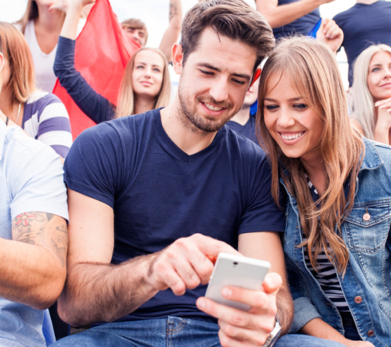 A couple sitting down in a crowd, looking at a mobile phone A couple sitting down in a crowd, looking at a mobile phone